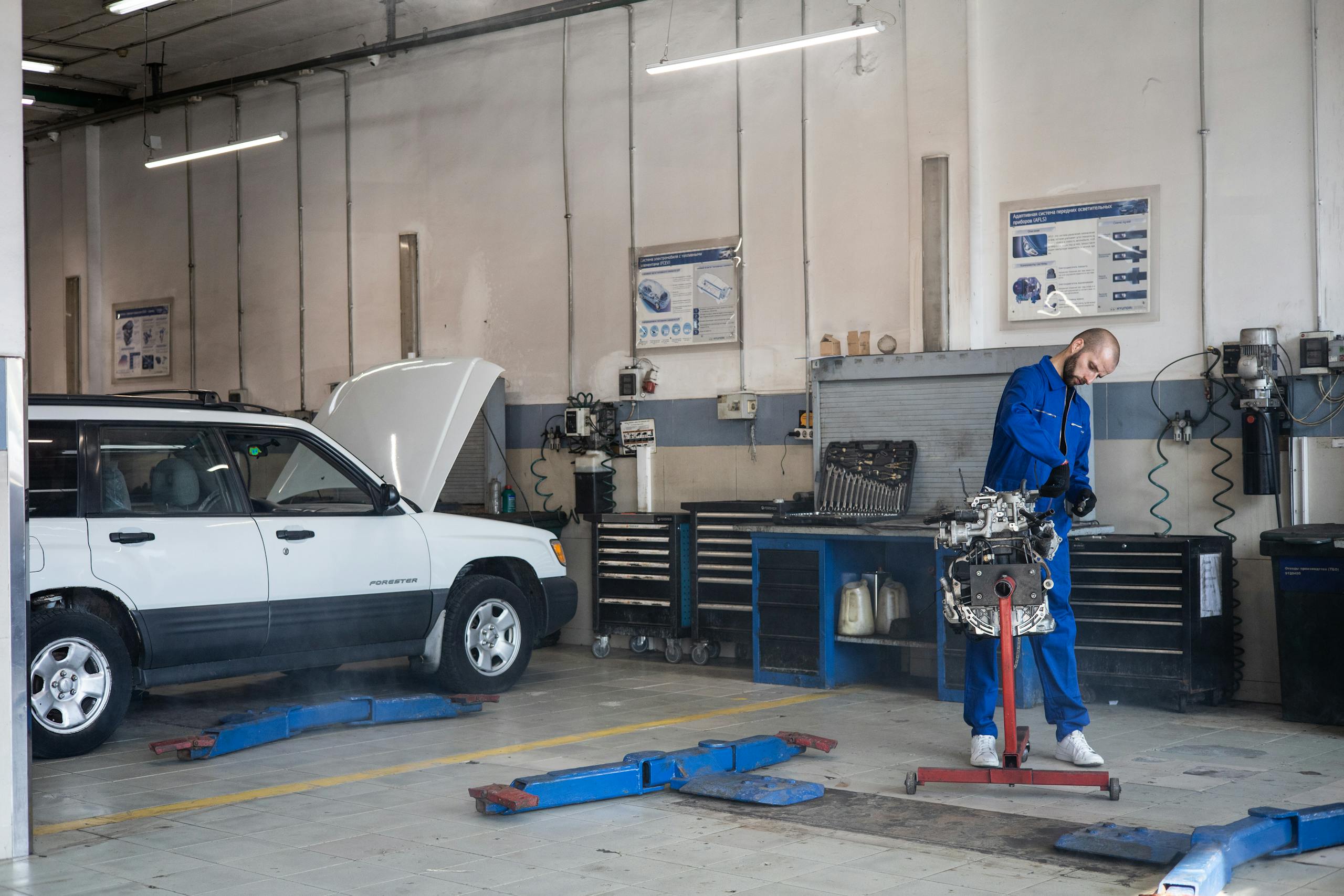 Mechanic in blue coveralls working on an engine in a modern auto repair workshop.